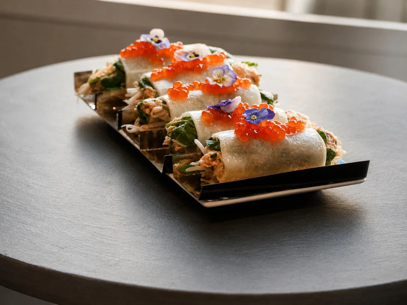 Rouleaux de printemps au tourteau, œufs de saumon et fleurs comestibles sur plateau noir — entrées du traiteur gastronomique Les Temps Gourmands à Pont-l'Abbé, Pays Bigouden